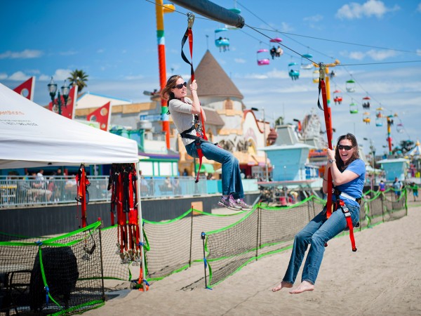 Corporate fun day out two ladies, both wearing jeans and t-shirts, having fun on a mobile zipline on a warm summers day at a fun fair