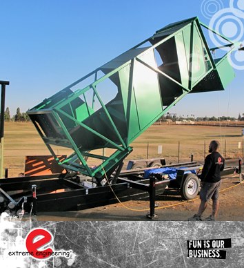 mobile zip wire hire tower The image features a mobile zip wire tower being erected in a field prior to a corporate event. The main zip wire tower is green in colour and is engineered from steel casing and cross braces