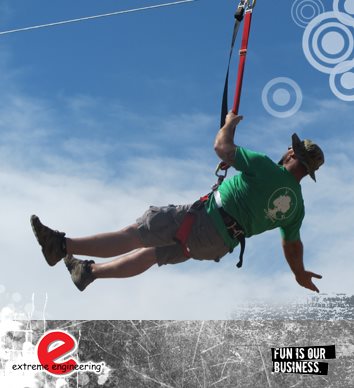 Mobile Zipwire Hire for events UK Man in a hat and green t-shirt, gliding down a zip line with a blue sky behind and a few fluffy white clouds